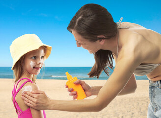 Mother applying sunscreen onto her daughter's skin at beach. Sun protection while outdoor...