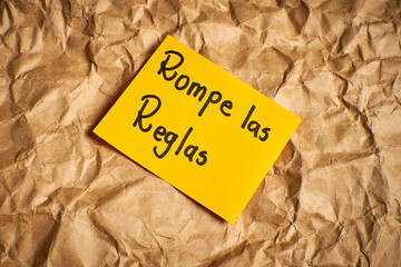 Spanish motivational phrase Break the rules handwritten on paper with colorful background