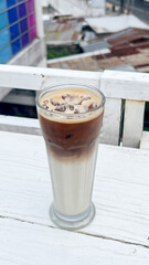 Cold iced coffee with milk on table in city background. Ice coffee in a tall glass with cream...