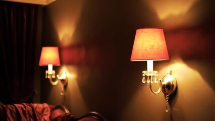 Two sconce lamps with red shades illuminate a dark brown wall