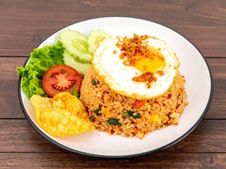 Classic Indonesian Nasi Goreng, a popular stir-fried rice dish, served with a crispy fried egg, crackers, and fresh vegetables on a wooden table.