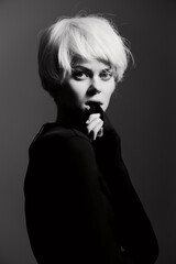 Pensive young woman with short blonde hair, dressed in a black outfit, gazing thoughtfully while...