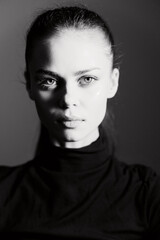 Thoughtful woman with striking features poses against a dark background, wearing a turtleneck,...