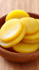 Pickled yellow radish slices in wooden bowl on wooden surface, showcasing fresh and appetizing texture