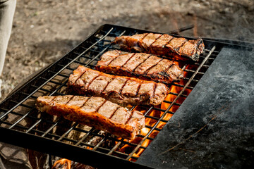 Beef steaks grilling on a cast iron grlill plate on a camp fire. Campfire cooking. Outdoor BBQ