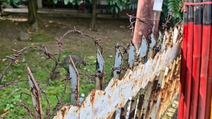 Rusty Barbed Wire Fence Against a Green Backdrop, Close-Up of an Old Barrier with Barbed Wire