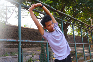 Fototapeta premium A man is stretching his arm in front of a fence. Concept of determination and focus as the man works on his flexibility