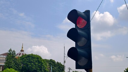 Traffic light showing red on a clear day, with a building in the distance,Traffic light on red against a blue sky with white clouds and a building with a dome in the background