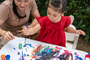 happy mother and toddler girl painting watercolor in paper at backyard.