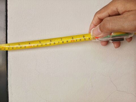 A man measures the surface of a wall with a measuring tape.