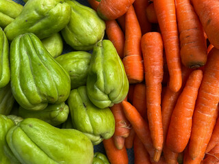A vibrant mix of fresh green chayotes and bright orange carrots.
