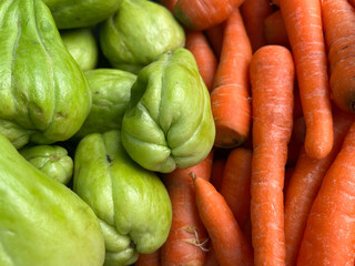 A vibrant mix of fresh green chayotes and bright orange carrots.