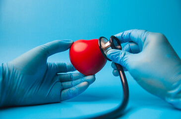 doctor uses a stethoscope to check the heartbeat.red heart shape exercise ball in hands with doctor physician's stethoscope on light blue background. world heart health day. doctor day.