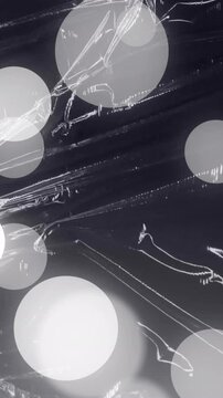 Animation of grey and white spots of light over light on moving shiny black plastic