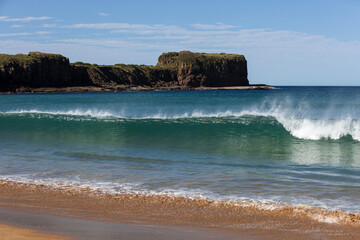 An aqua coloured wave breaks on the shore of Bombo Beach, just north of the beautifully scenic...