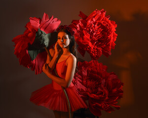 Close-up portrait of ballerina holding oversized red flower in golden light, brunette model in red...