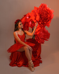 Close-up portrait of ballerina holding oversized red flower in golden light, brunette model in red...