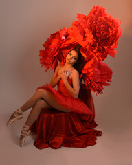 Close-up portrait of ballerina holding oversized red flower in golden light, brunette model in red...