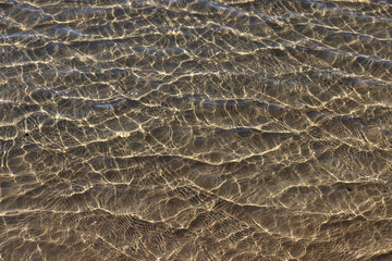 Mesmerising natural liquid patterns of crystal clear ocean water glistening in the shallows of an idyllic clean shoreline. 