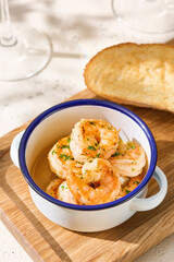 Shrimp with garlic in enamel bowl, bright overhead, rustic wooden board composition