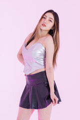 Asian pretty young woman model standing pose playfully confident under purple neon lighting wearing silver corset top black pleated leather skirt trendy streetwear style creating fashion in studio.