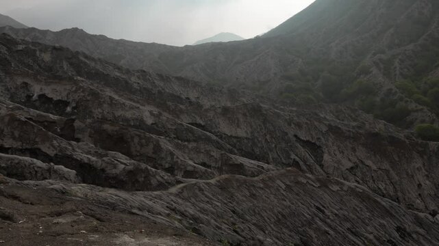 Mount Batok rugged terrain in East Java, Indonesia, revealing volcanic ash ridges and patches of greenery giving brown-green tones under misty sky.