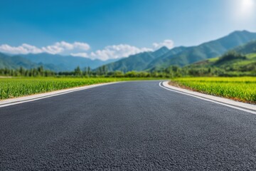 Fototapeta premium Empty asphalt road winding through green meadows with mountain landscape in background on sunny summer day