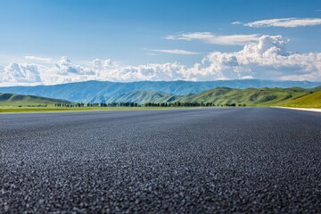 Empty asphalt road crossing a green valley with a mountain range and blue sky with clouds in the background