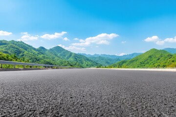 Asphalt highway leading through a green valley surrounded by mountains under a bright blue sky with some clouds
