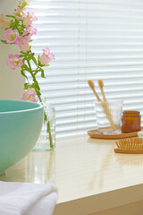 Bright bathroom with pastel green sink, pink flowers, wooden tray, and towel roll. Clear surface...