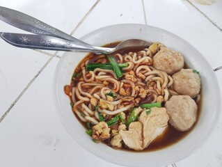 Bowl of Indonesian meatball noodle soup with hot broth. Served in a white bowl with spoon and fork...