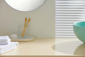 Minimalist bathroom with folded towels, green glass cup holding toothbrushes, and pastel sink....