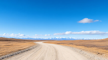 Fototapeta premium A scenic dirt road winds through a vast landscape under a clear blue sky, evoking tranquility and adventure in nature's beauty.