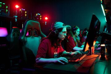 Group of Caucasian and multiethnic teenage girls sitting at gaming computers wearing headsets...