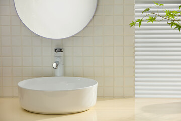 Modern bathroom with round white sink, circular mirror, and bright blinds. Clean surface with tiled...