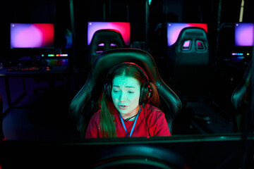 Caucasian teenage girl gamer wearing headset sitting in front of computer monitor concentrating on playing video game in e-sports arena- © pressmaster