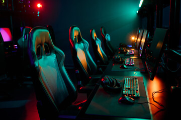 Row of empty gaming chairs and computer setups arranged in esports arena, headsets resting on...