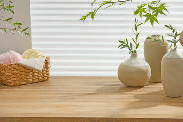 Bathroom counter with natural wicker basket, ceramic vases, soft foliage, and wood grain surface....