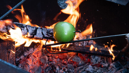 Apple on a scewer roasting over a campfire pit with bright orange flames 