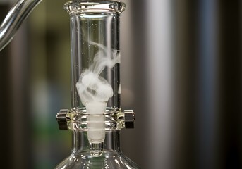 Close-up of a glass condenser tube with white vapor rising inside during a scientific experiment or process