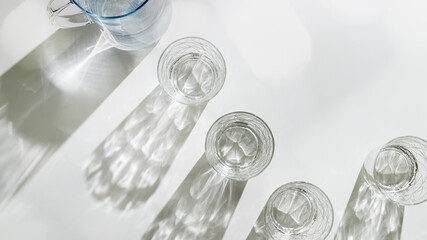 Water Glasses and water jug with Shadows and sunlight Reflection on white background, colored photo...