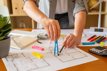 Architect working on a sustainable building project, drawing blueprints with a compass and pencil, surrounded by tools and a miniature wind turbine model