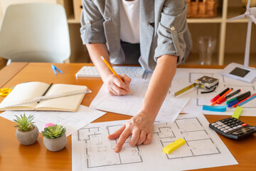 Architect working on a sustainable building project, reviewing blueprints and focusing on...