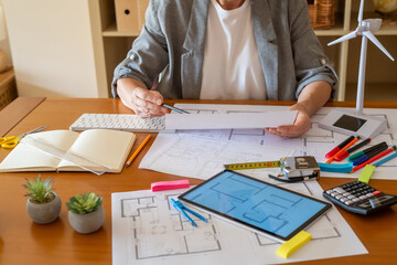 Architect reviews blueprints for an ecological construction project, incorporating renewable energy...