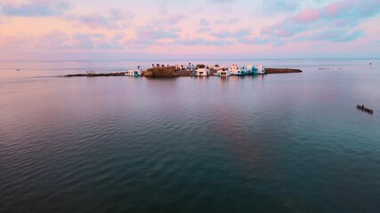 A group of small houses and a beach resort on top of a small island. The island is surrounded by blue waters with clouds in the sky above it. Location: Tunisia, Medenine , Zarzis.