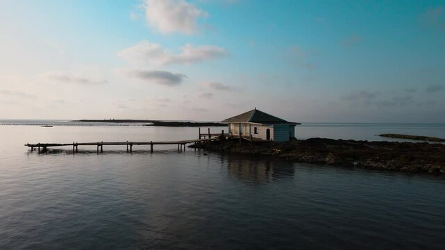 A small island with a wooden house and dock on it, surrounded by calm water. Location: Tunisia, Medenine , Zarzis.