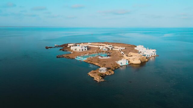 An island in a body of water with blue houses and sandy beach. Location: Tunisia, Medenine , Zarzis.
