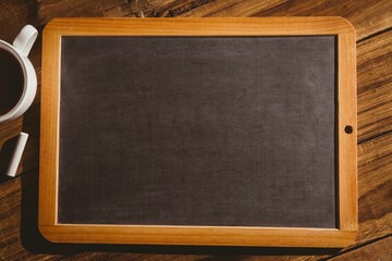 Flat design wooden-framed chalkboard is resting on dark wooden table with chalk and coffee cup