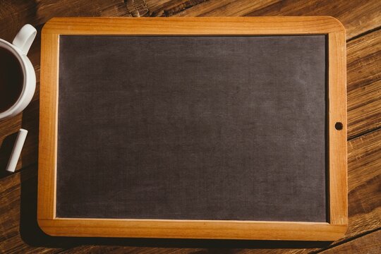 Flat design wooden-framed chalkboard is resting on dark wooden table with chalk and coffee cup