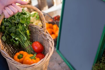 Hand holding a basket full of vegetables in a market